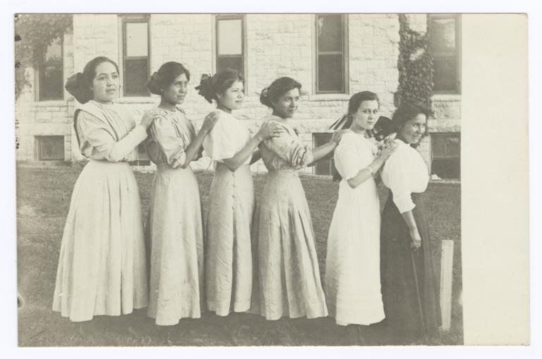 Six Young Women Standing in Size Order Outside; a Stone Building Is Backdrop