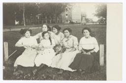 Six Young Women Sitting on a Low Bench on the Lawn
