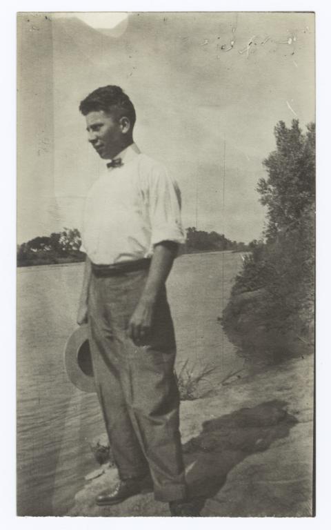 Young Man Holding a Hat Standing by a Lake