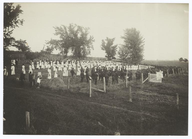 Large Group of People on a Field, Marching Band in Uniform on one Side and  Women in White Dresses