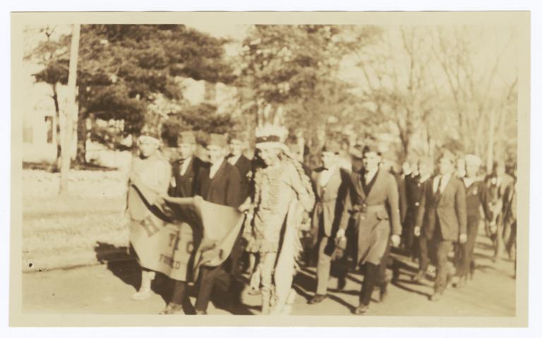 Haskell Institute Members Marching in a Parade, in Native American Dress, Holding School Banner