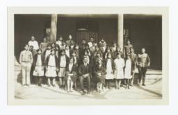 Large Group of Unidentified People in front of a Building, Three Adults Seated in Front Row