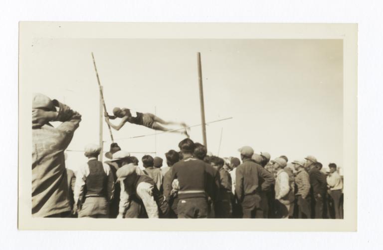 At a Track and Field Sporting Event, a Man in the Midst of the High Jump Surrounded by Crowd