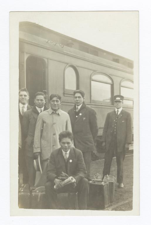 Five Men with Luggage Standing next to a Train and Conductor