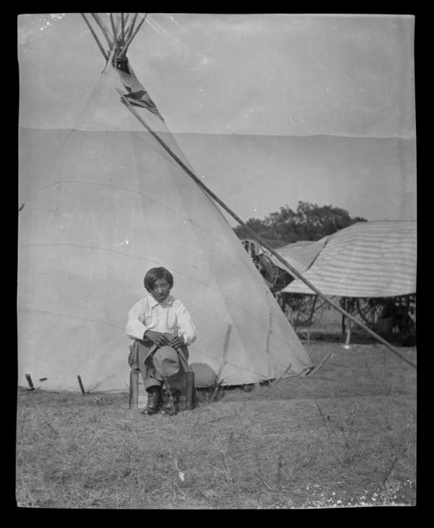 American Indian Boy With a Hat Sitting in front of a Tipi