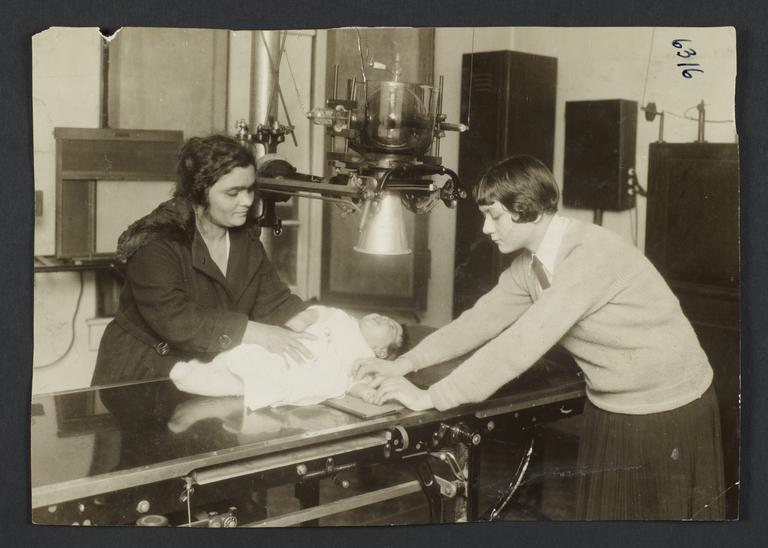 Mulberry Health Center Album -- Two Women Holding Baby on Examining Table
