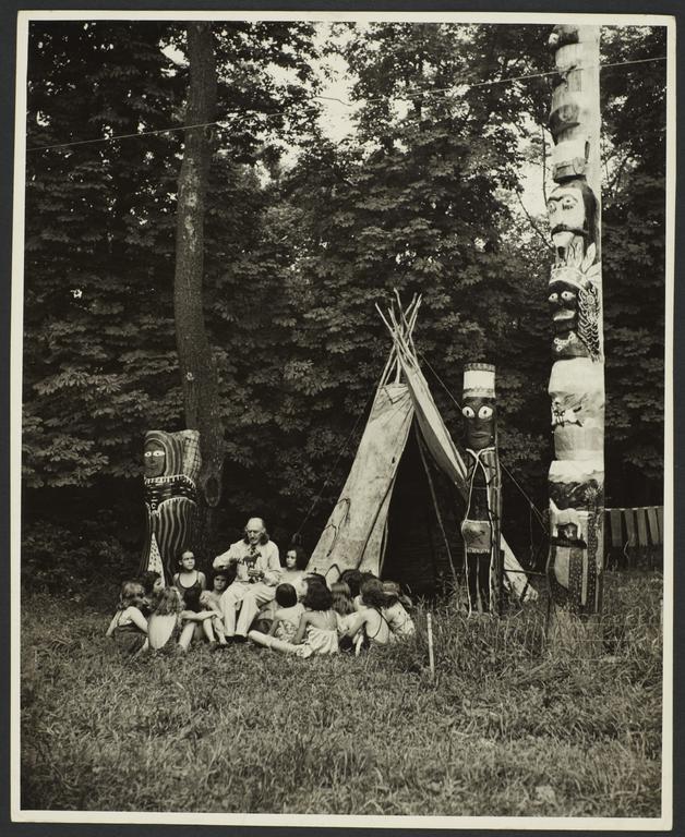 "Bronco" Charlie with Group of Children near Teepee and Totem Poles